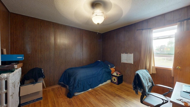 bedroom with wood finished floors, wooden walls, a textured ceiling, and ceiling fan