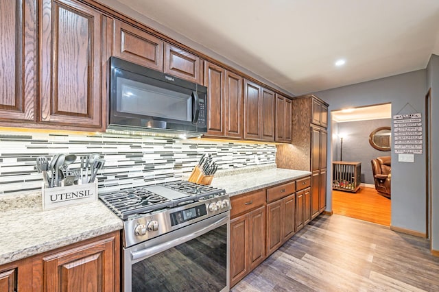 114 3rd Ave E, Truman, MN 56088 - kitchen featuring black microwave, stainless steel range with gas stovetop, tasteful backsplash, light wood-style flooring, and baseboards