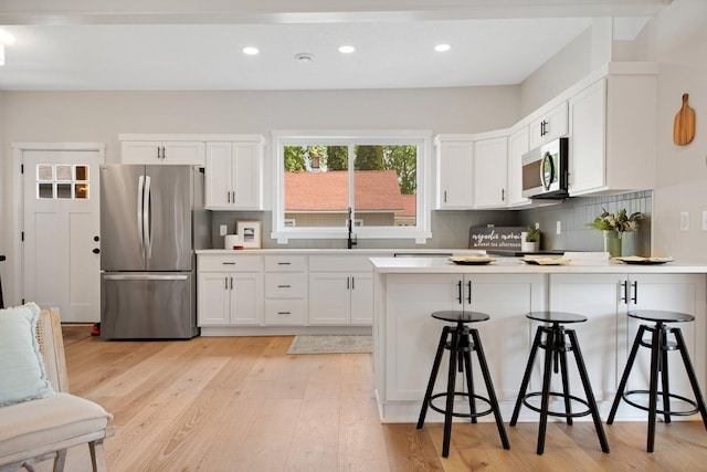 309 Shore Dr, Forest Lake, MN 55025 - kitchen featuring stainless steel appliances, a peninsula, white cabinetry, a breakfast bar area, and decorative backsplash
