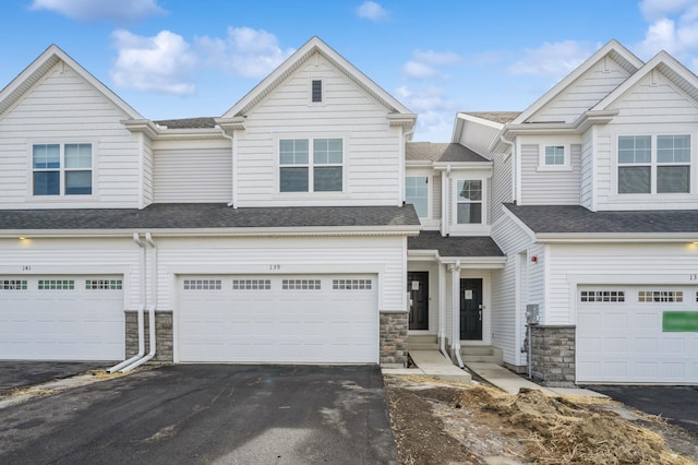 multi unit property featuring asphalt driveway, stone siding, a garage, and a shingled roof