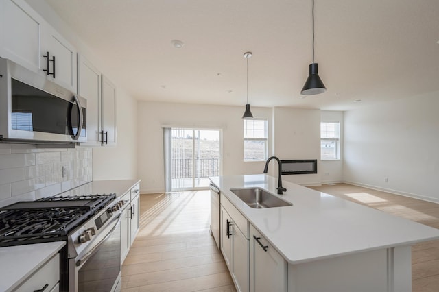 kitchen featuring stainless steel appliances, a sink, light wood-type flooring, backsplash, and open floor plan