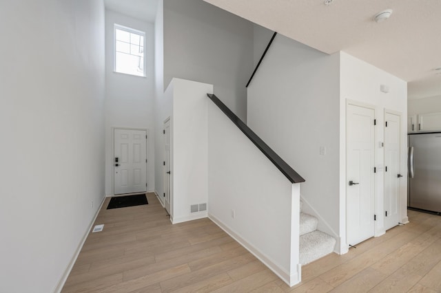 foyer featuring light wood-style floors, baseboards, stairs, and a high ceiling