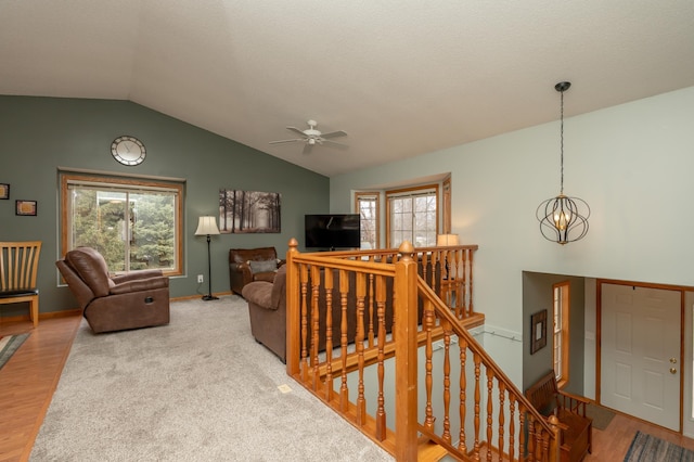 living area with lofted ceiling, ceiling fan, plenty of natural light, wood finished floors, and a chandelier