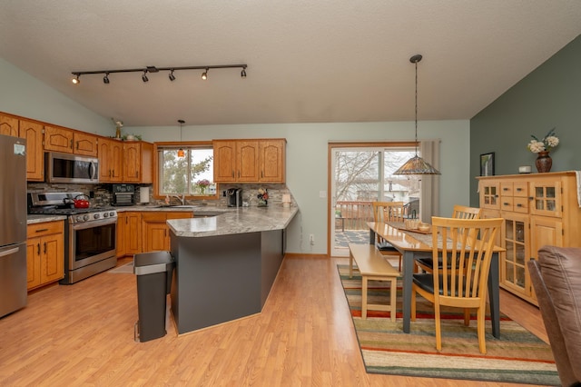 kitchen with appliances with stainless steel finishes, a sink, decorative backsplash, a peninsula, and light wood finished floors