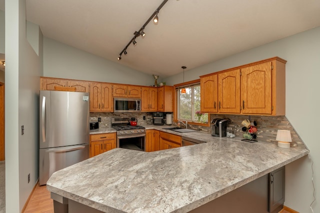 kitchen with appliances with stainless steel finishes, a sink, light countertops, a peninsula, and vaulted ceiling