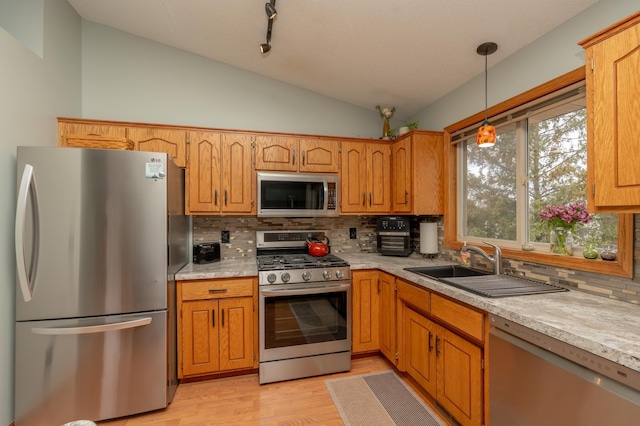 kitchen with appliances with stainless steel finishes, vaulted ceiling, tasteful backsplash, a sink, and light countertops
