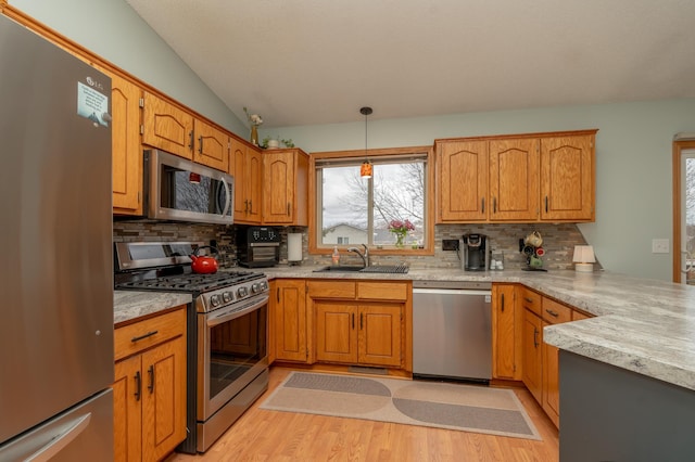 kitchen with appliances with stainless steel finishes, a sink, light wood-style flooring, decorative backsplash, and light countertops