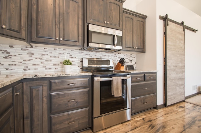 8259 Barton Ave NW, Buffalo, MN 55313 - kitchen with stainless steel appliances, light wood finished floors, a barn door, dark brown cabinetry, and tasteful backsplash
