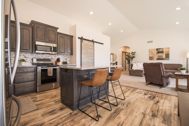 8259 Barton Ave NW, Buffalo, MN 55313 - kitchen featuring appliances with stainless steel finishes, arched walkways, dark brown cabinetry, vaulted ceiling, and a kitchen island