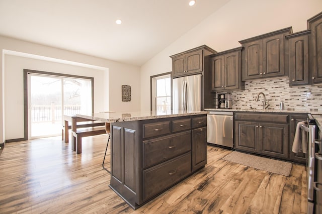 8259 Barton Ave NW, Buffalo, MN 55313 - kitchen featuring appliances with stainless steel finishes, vaulted ceiling, tasteful backsplash, light stone counters, and a center island