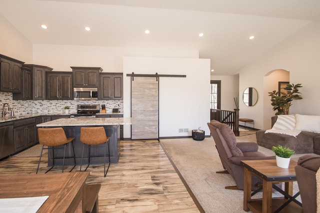 8259 Barton Ave NW, Buffalo, MN 55313 - kitchen with stainless steel appliances, dark brown cabinetry, recessed lighting, a kitchen bar, and light wood-style flooring