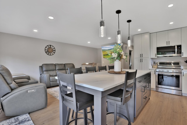 8466 Isleton Ct S, Cottage Grove, MN 55016 - kitchen with stainless steel appliances, a kitchen breakfast bar, light wood finished floors, hanging light fixtures, and recessed lighting