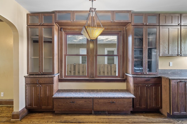 unfurnished dining area featuring arched walkways, dark wood-type flooring, and baseboards