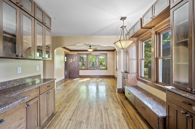 unfurnished dining area with arched walkways, light wood-style floors, baseboards, and ceiling fan