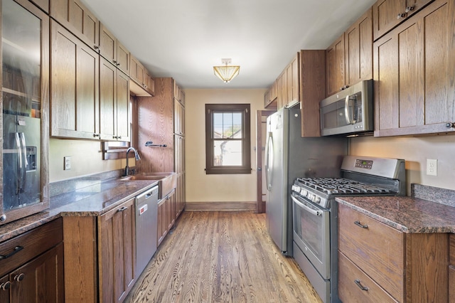 kitchen with stainless steel appliances, a sink, light wood-style floors, baseboards, and dark stone countertops