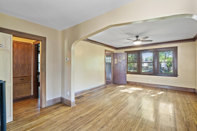 unfurnished room with baseboards, arched walkways, light wood finished floors, and ornamental molding