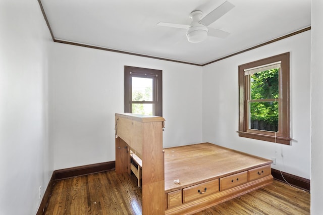 unfurnished bedroom with ornamental molding, wood finished floors, baseboards, and a ceiling fan