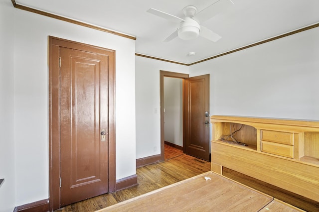 unfurnished bedroom with crown molding, wood finished floors, baseboards, and a ceiling fan