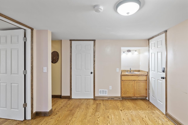 unfurnished bedroom with a sink, light wood finished floors, baseboards, and ensuite bath