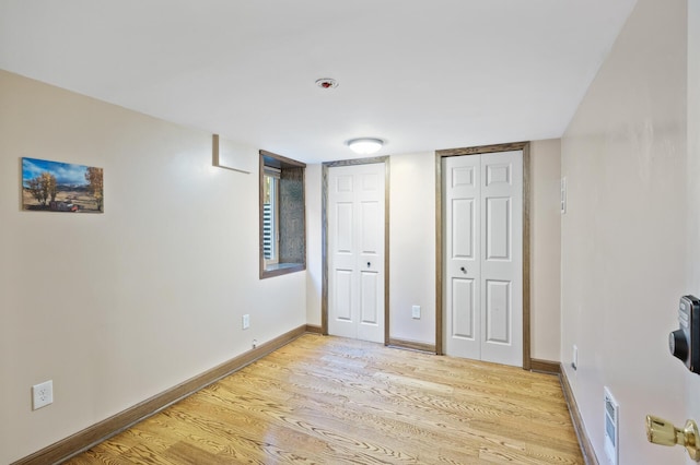 unfurnished bedroom with multiple closets, light wood-type flooring, and baseboards