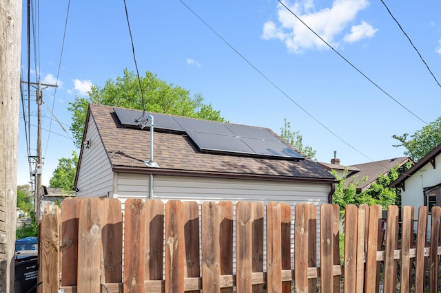 view of side of property with roof mounted solar panels, roof with shingles, and fence