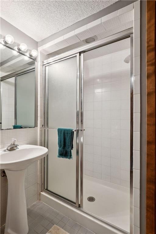 745 Virginia Shores Cir, Victoria, MN 55331 - bathroom featuring tile patterned flooring, a shower stall, a textured ceiling, and tile walls