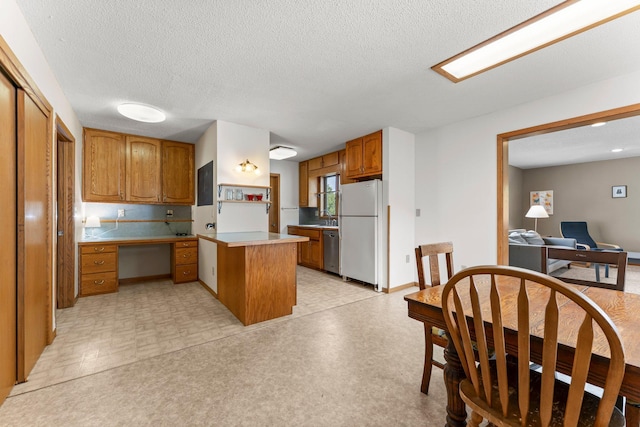 1231 135th St, Amery, WI 54005 - kitchen featuring freestanding refrigerator, stainless steel dishwasher, a peninsula, brown cabinetry, and an office area