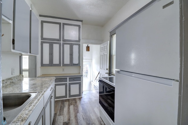 1010 University Dr N, Fargo, ND 58102 - kitchen featuring freestanding refrigerator, range with electric cooktop, wood finished floors, light countertops, and glass insert cabinets