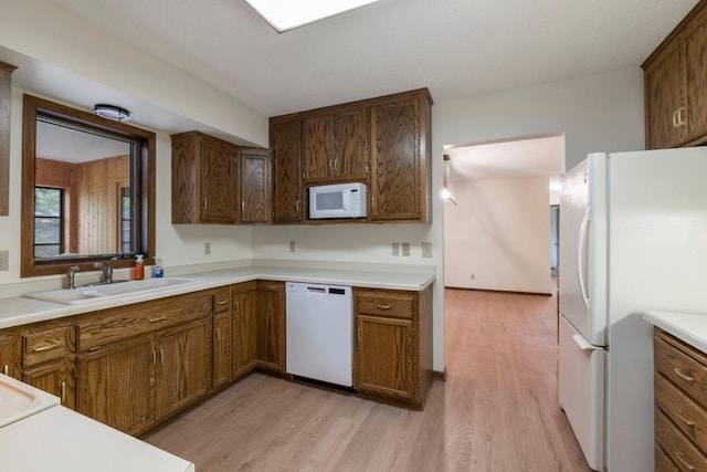 kitchen with white appliances, a sink, light wood-type flooring, and light countertops