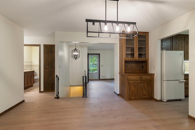 kitchen with freestanding refrigerator, a chandelier, light wood finished floors, brown cabinetry, and glass insert cabinets