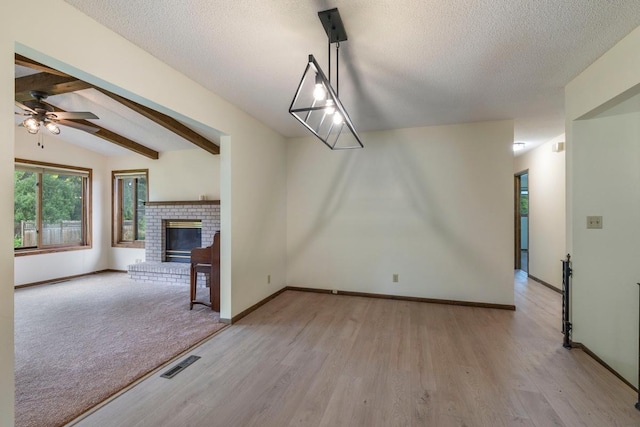 unfurnished dining area featuring wood finished floors, a textured ceiling, ceiling fan, a fireplace, and baseboards