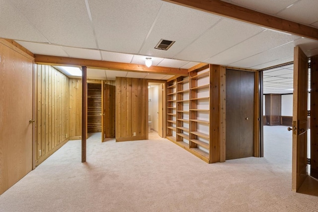 finished below grade area with carpet flooring, wooden walls, a paneled ceiling, and built in shelves