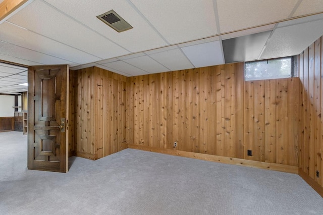 below grade area with carpet, wood walls, and a paneled ceiling