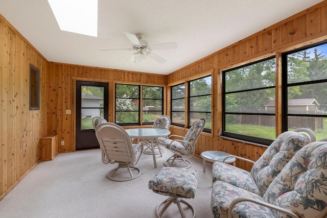 living room featuring wood walls, healthy amount of natural light, carpet floors, ceiling fan, and a skylight