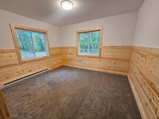 spare room featuring baseboard heating, wainscoting, wooden walls, and dark carpet
