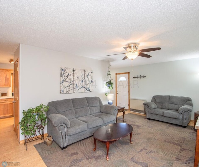 living area featuring ceiling fan, a textured ceiling, baseboards, and light wood finished floors