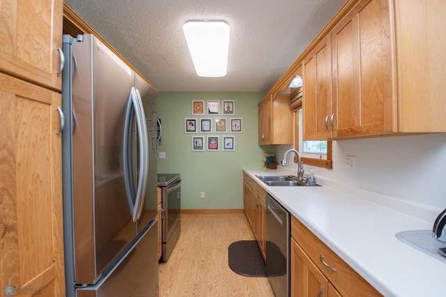 kitchen featuring appliances with stainless steel finishes, a sink, a textured ceiling, light countertops, and light wood-type flooring