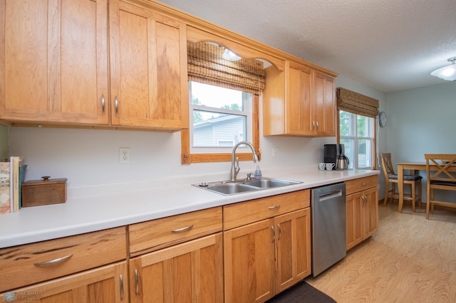 kitchen with stainless steel dishwasher, a sink, a textured ceiling, light countertops, and light wood-type flooring