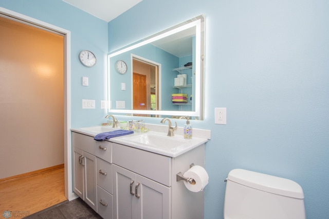 bathroom with toilet, double vanity, and wood finished floors