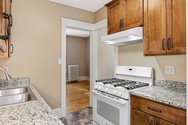 2227 Garfield Ave, Minneapolis, MN 55405 - kitchen featuring white gas range, radiator, under cabinet range hood, a sink, and brown cabinets