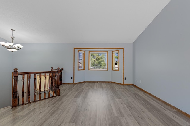 spare room featuring light wood finished floors, a chandelier, and baseboards