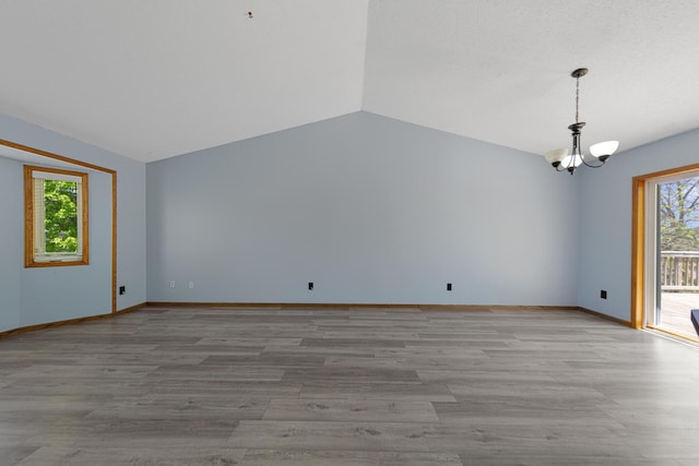 empty room featuring a chandelier, lofted ceiling, light wood finished floors, and baseboards
