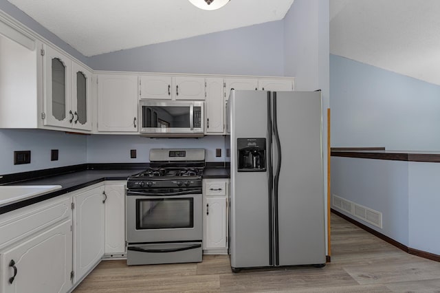 kitchen featuring stainless steel appliances, vaulted ceiling, dark countertops, white cabinetry, and light wood-type flooring