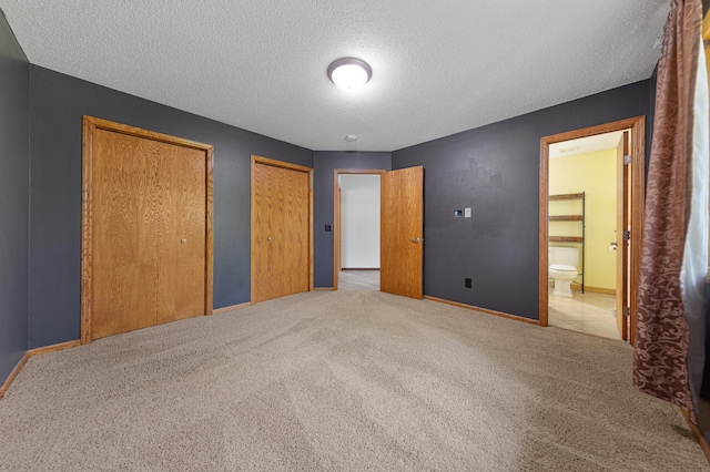 unfurnished bedroom with multiple closets, carpet floors, a textured ceiling, baseboards, and ensuite bath