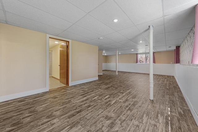 below grade area with wood finished floors, a drop ceiling, and baseboards