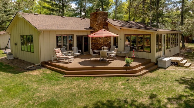 rear view of property featuring a chimney, roof with shingles, a deck, and a lawn