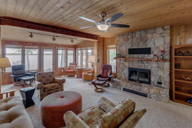 carpeted living room featuring wood walls, a stone fireplace, wood ceiling, and a ceiling fan