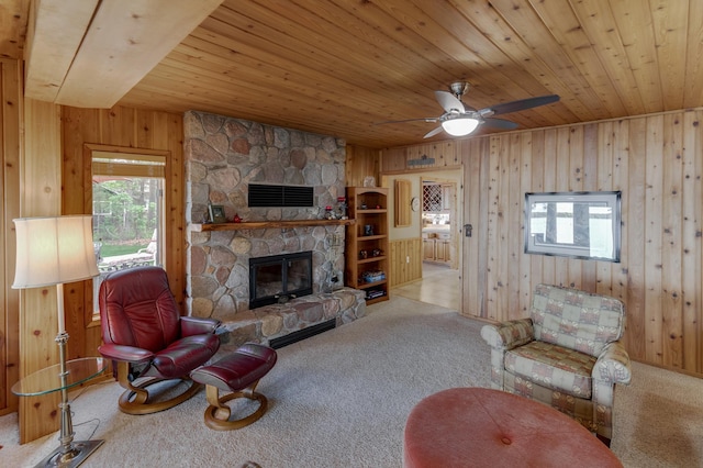 carpeted living room featuring wooden ceiling, healthy amount of natural light, wood walls, a stone fireplace, and a ceiling fan