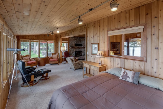 carpeted bedroom featuring wooden walls, lofted ceiling, rail lighting, a fireplace, and wood ceiling
