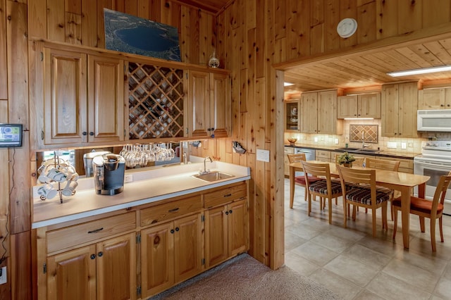 kitchen with white appliances, backsplash, a sink, wooden walls, and wooden ceiling